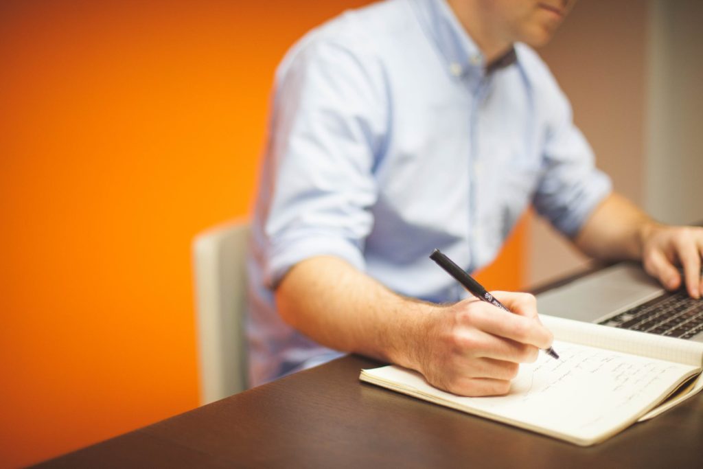 Man taking notes as he reviews content on his computer